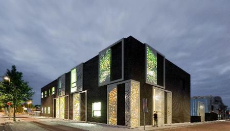 Gebouw Speciaal Onderwijs zog Heldringschool. Donker gebouw met verlichte ramen, groen en warm witlicht.