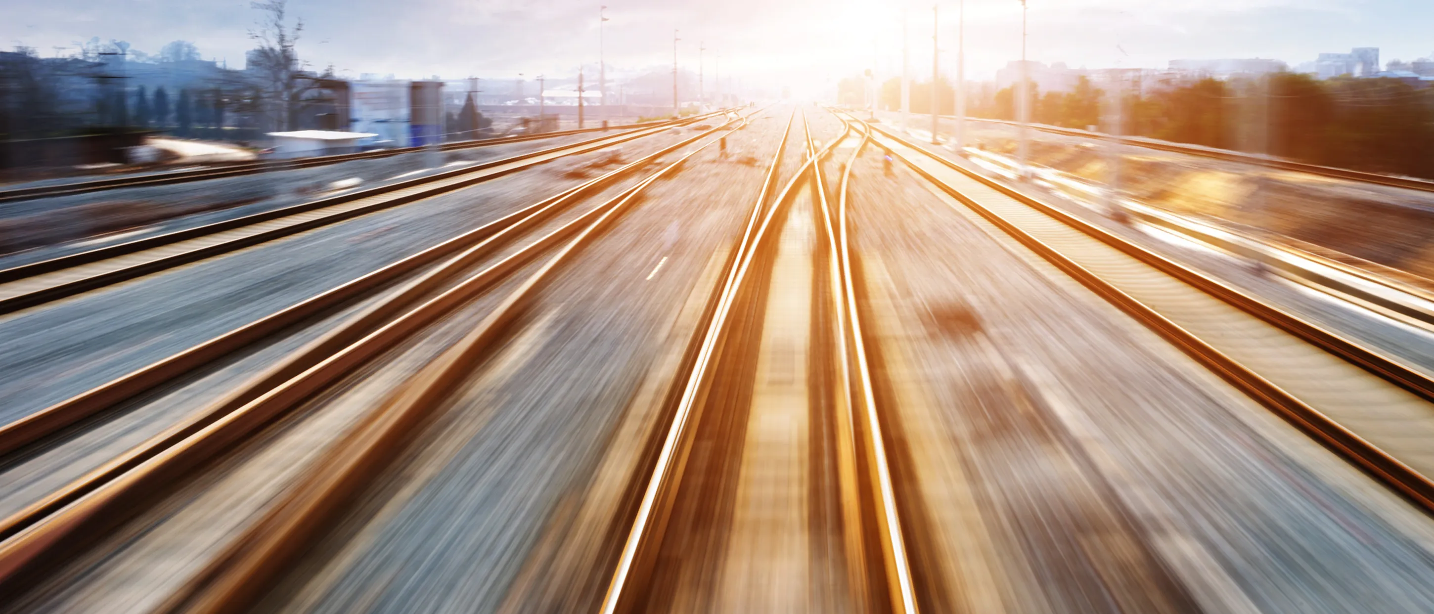 Une photo prise depuis un train en marche avec vue sur les voies et soleil flou en arrière­plan.