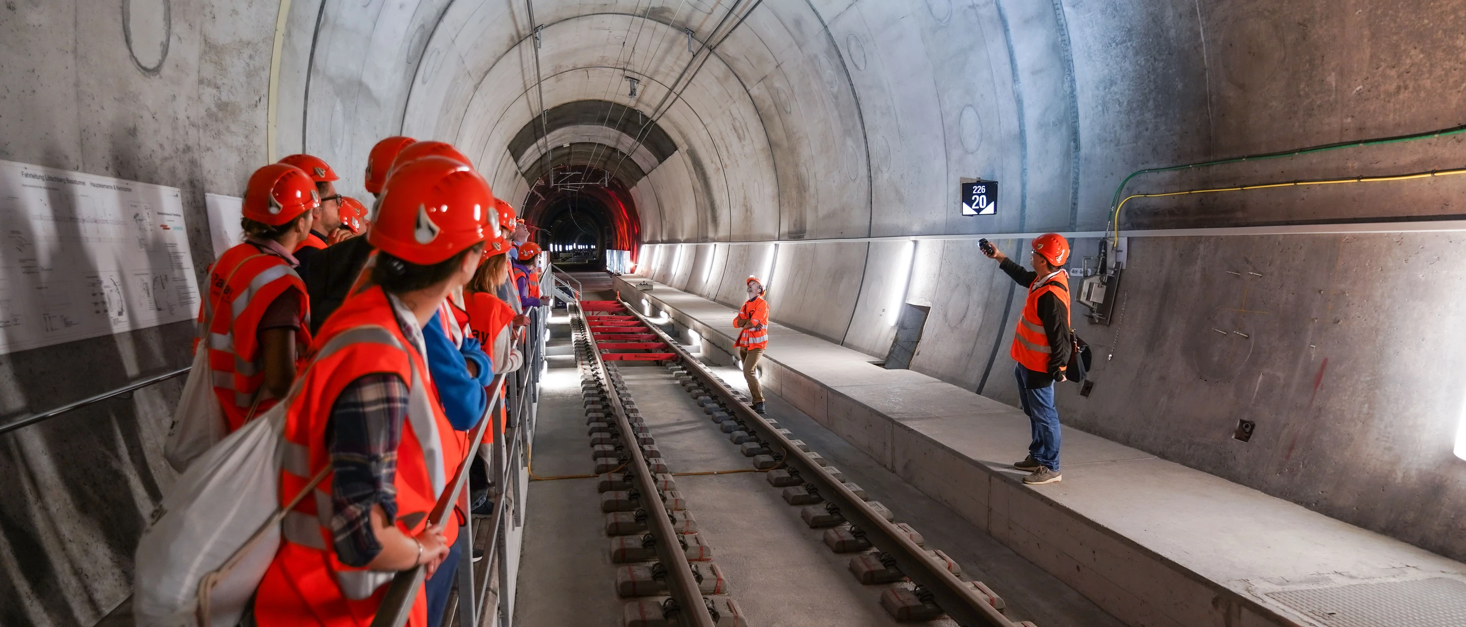 Des personnes portant casques et gilets de sécurité orange se trouvent dans un tunnel.