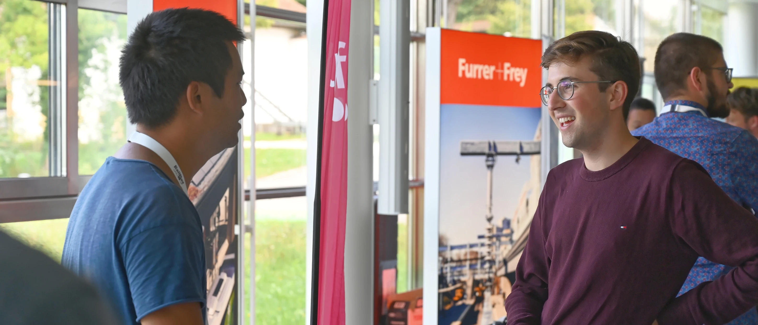 Deux jeunes hommes ont une conversation amicale à un stand d’exposition.