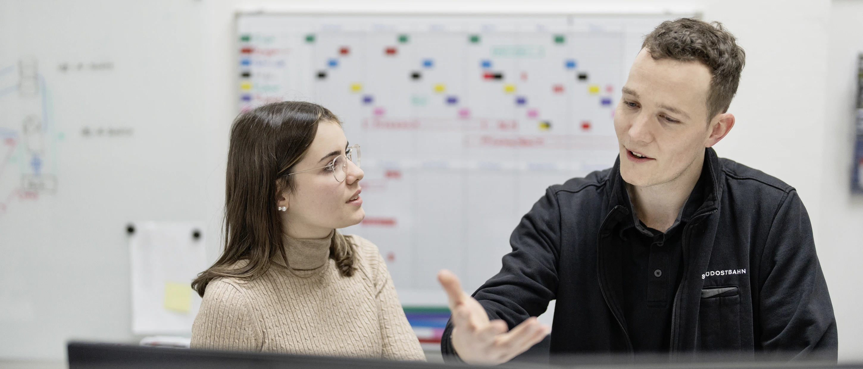 A man and a woman are talking in front of a computer in an office.