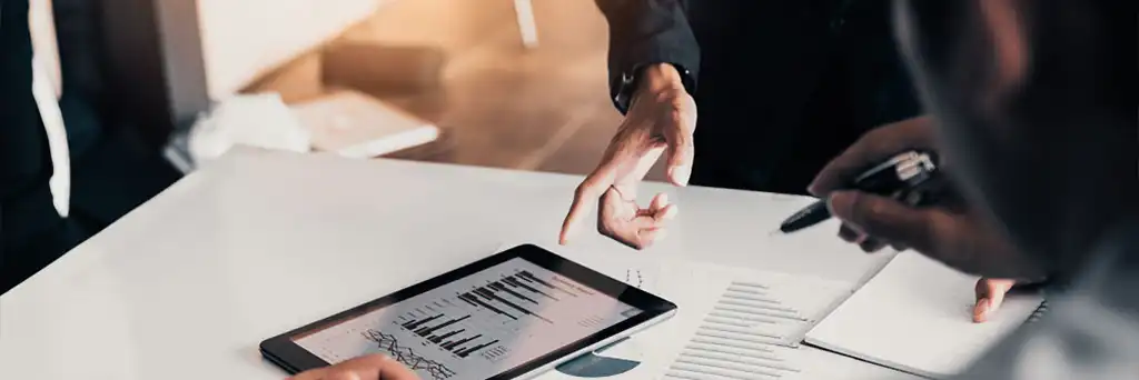 Drei Personen an einem Tisch, auf dem Tablet und Diagramme liegen