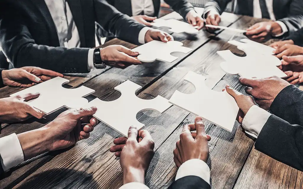 Mehrere Hände, die Puzzleteile halten, als Symbolbild für Segregation of Duties (Funktionstrennung)