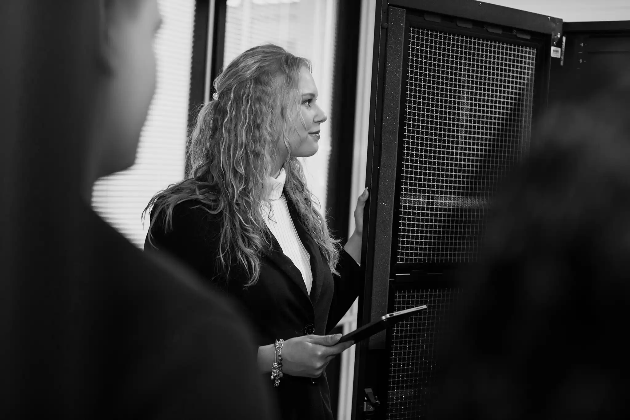 A professional woman in a business suit standing in front of a server, managing technology infrastructure.