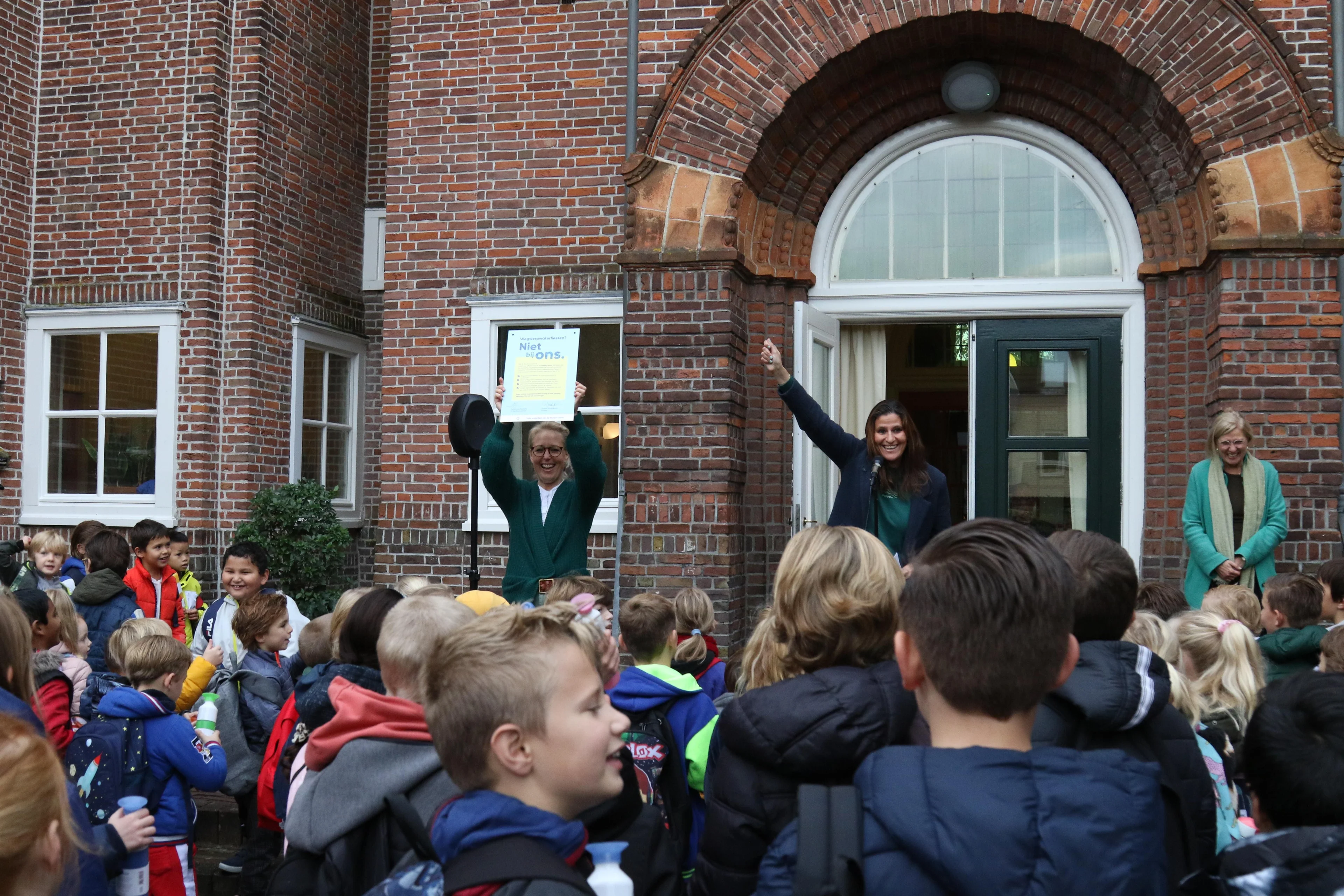 People and kids in front of a school holding up the Dopper Wave sign