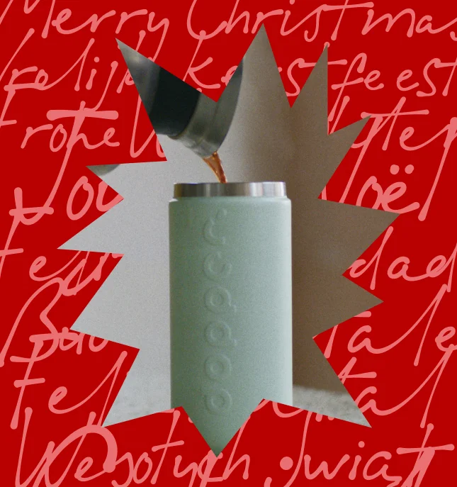A green Dopper Travel Mug being filled with coffee, with a red graphical frame with "Merry Christmas" written in different languages.