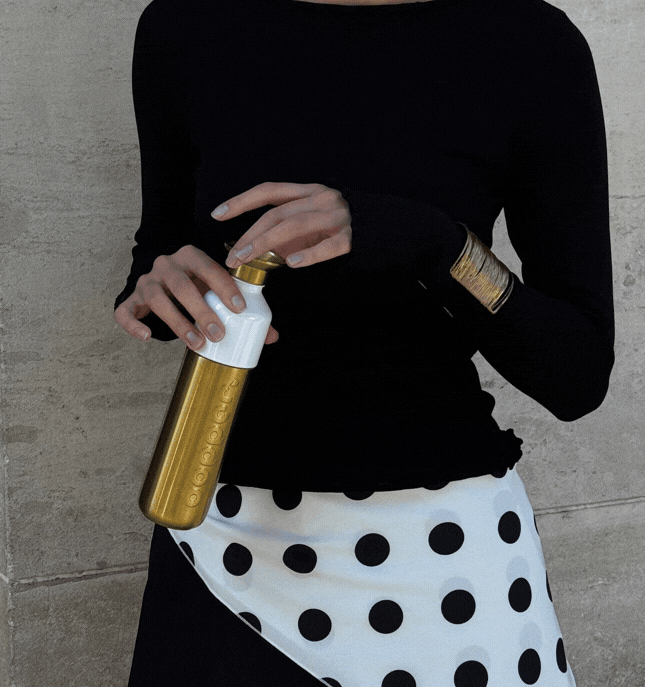 A woman dressed in black and white, holding a Dopper Steel Gold bottle, with text showing on the image: 90% recycled steel / Leakproof / Lightweight