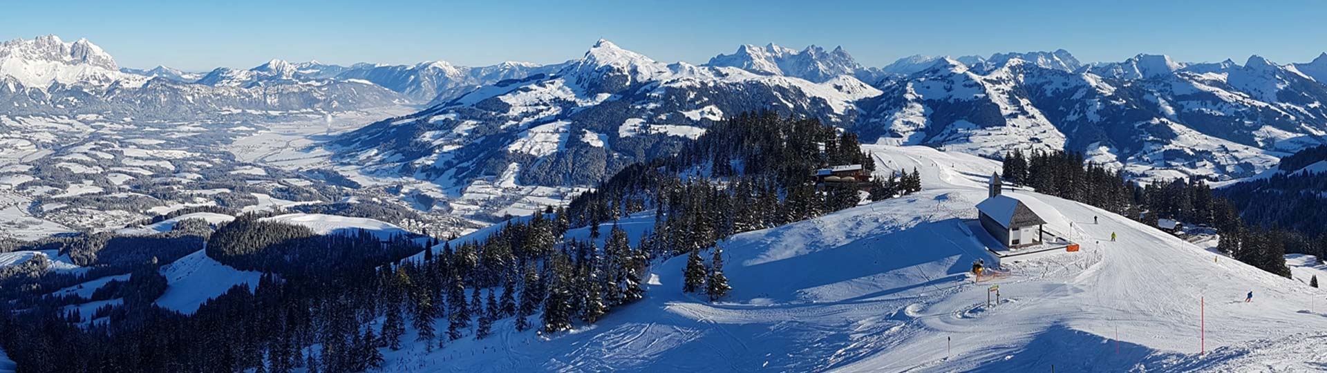 Winterliches Panorama verschneiter Kitzbüheler Skipisten mit weiter alpiner Landschaft – typisches Einsatzgebiet der Bergrettung Kitzbühel, die hier während des Hahnenkammrennens per websms verlässliche SMS-Nachrichten zur Einsatzkoordination versendet.