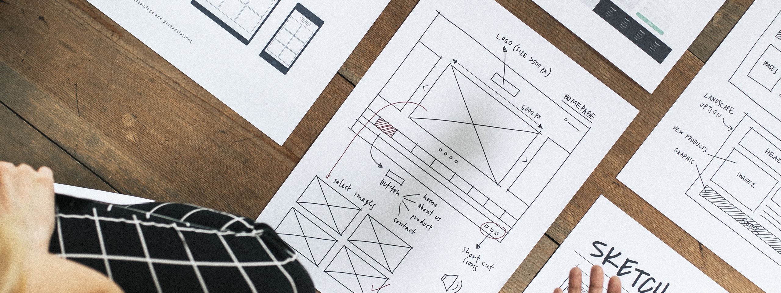 Zwei Personen besprechen Wireframes und Designskizzen für eine responsive Website, ausgebreitet auf einem Holzboden.