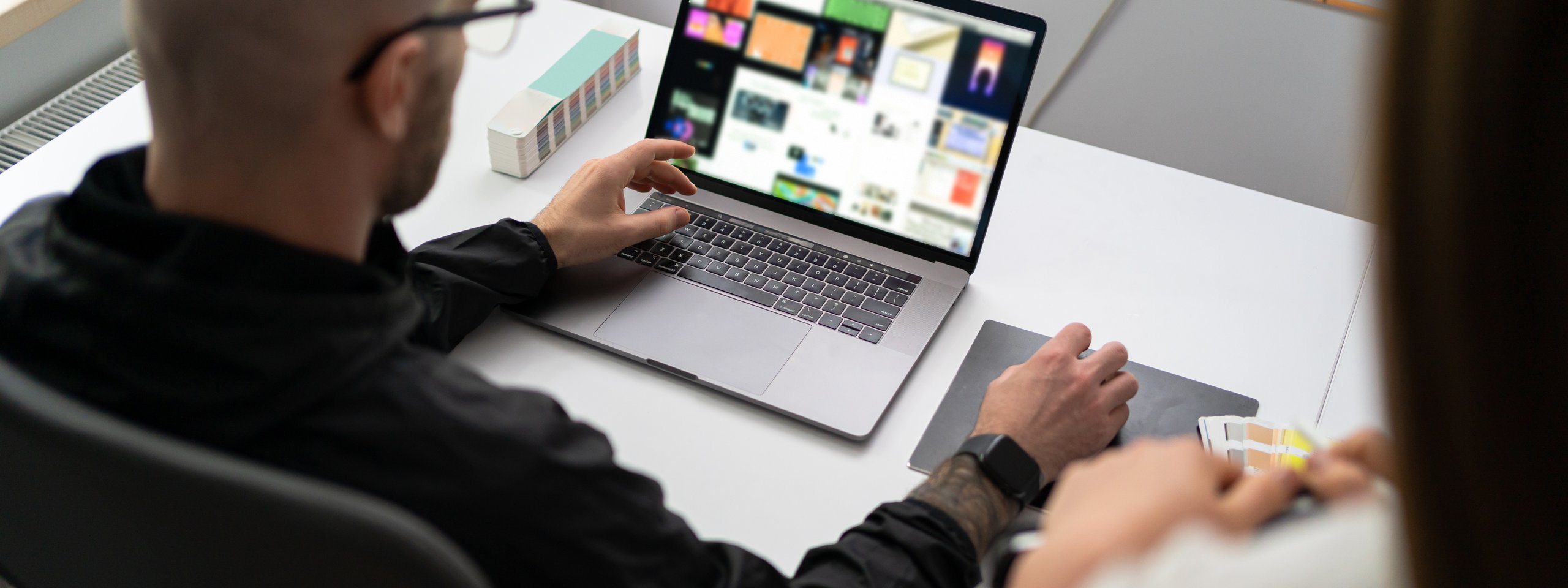 Designer arbeitet am Laptop mit Farbmusterkarten auf dem Tisch in einem modernen Büro.