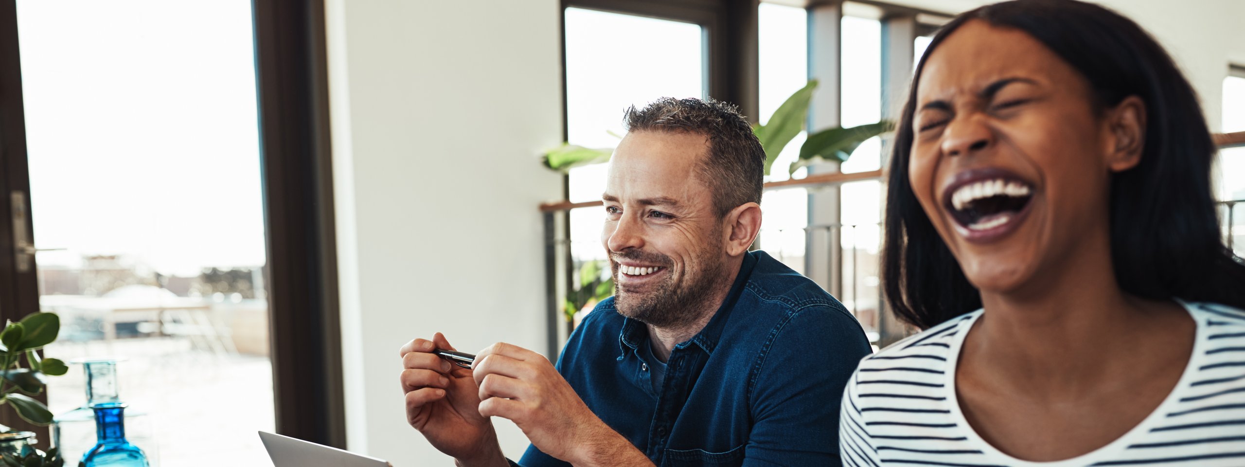Zwei Kollegen lachen gemeinsam bei einem lockeren Meeting im Büro.