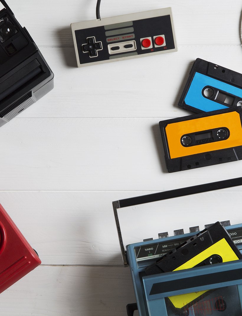 Retro-Gegenstände auf weißem Hintergrund: Polaroidkamera, alte Spielcontroller, Kassetten, Walkman-Kopfhörer und ein tragbares Radio.