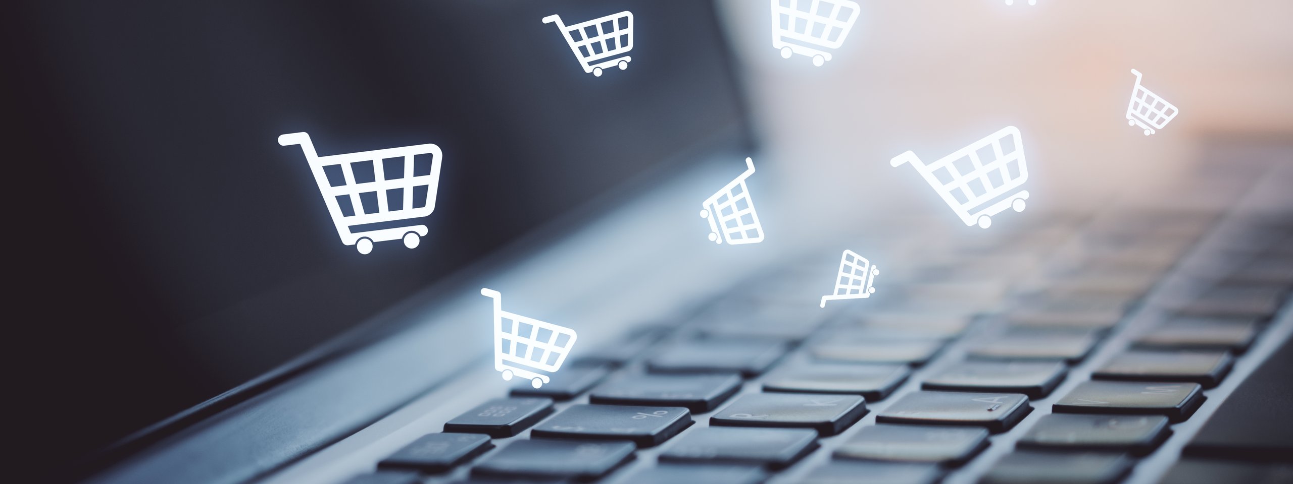 Laptop keyboard with digital shopping cart icons floating above, representing online shopping.