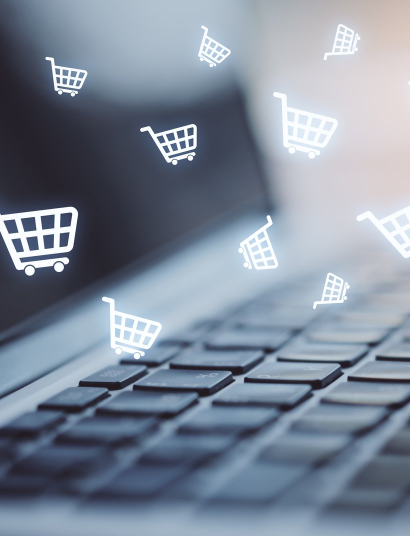 Laptop keyboard with digital shopping cart icons floating above, representing online shopping.