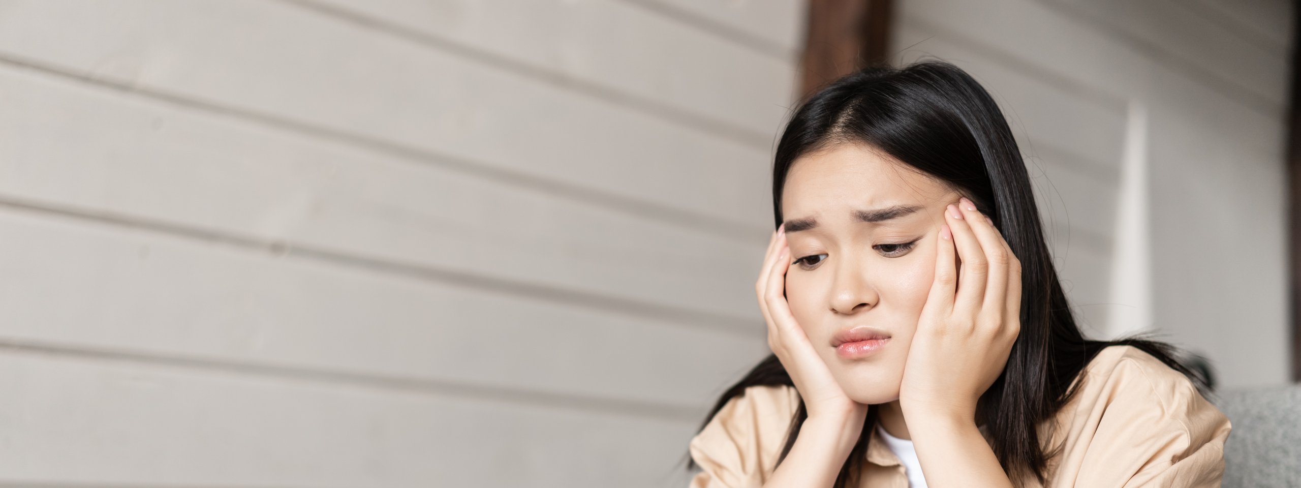 Junge Frau sitzt erschöpft vor einem Laptop und stützt nachdenklich den Kopf mit beiden Händen.