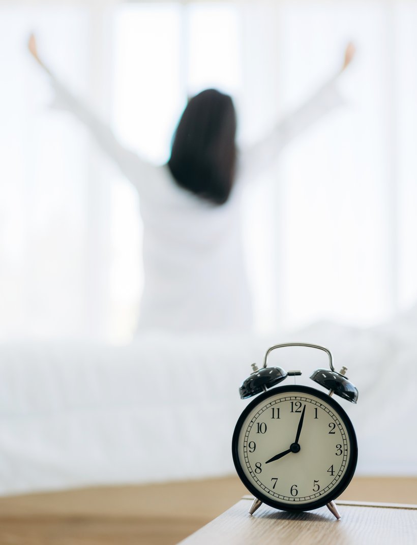 Nahaufnahme des Weckers auf dem Nachttisch. Junge Frau wacht glücklich auf .