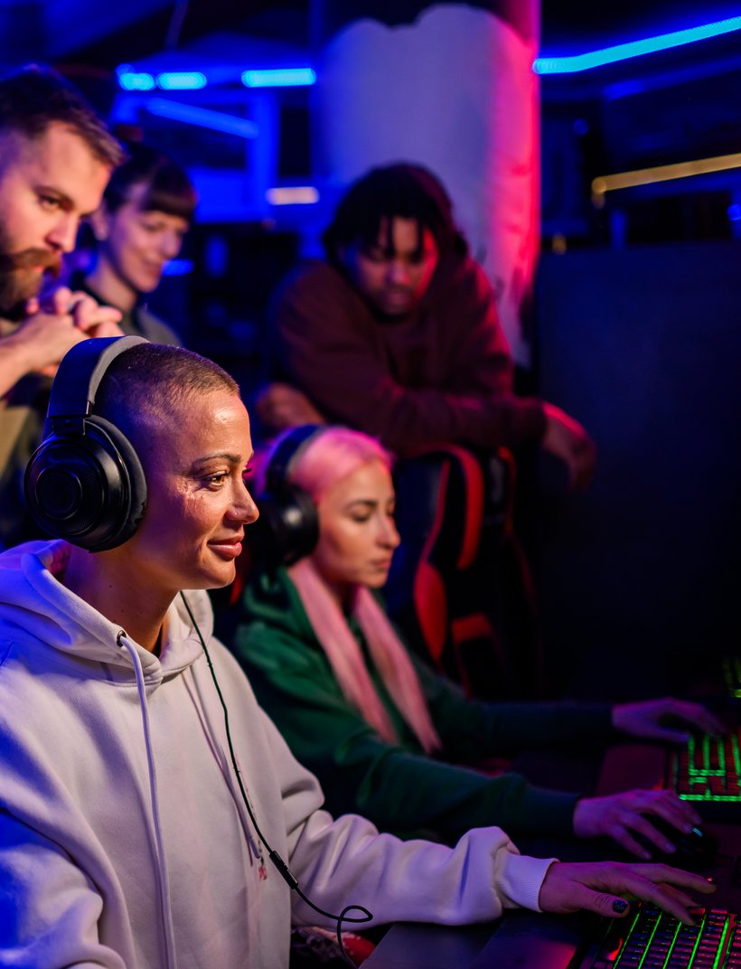 Gruppe junger Menschen spielt konzentriert Computerspiele an PCs in einer Gaming-Lounge mit buntem Neonlicht.