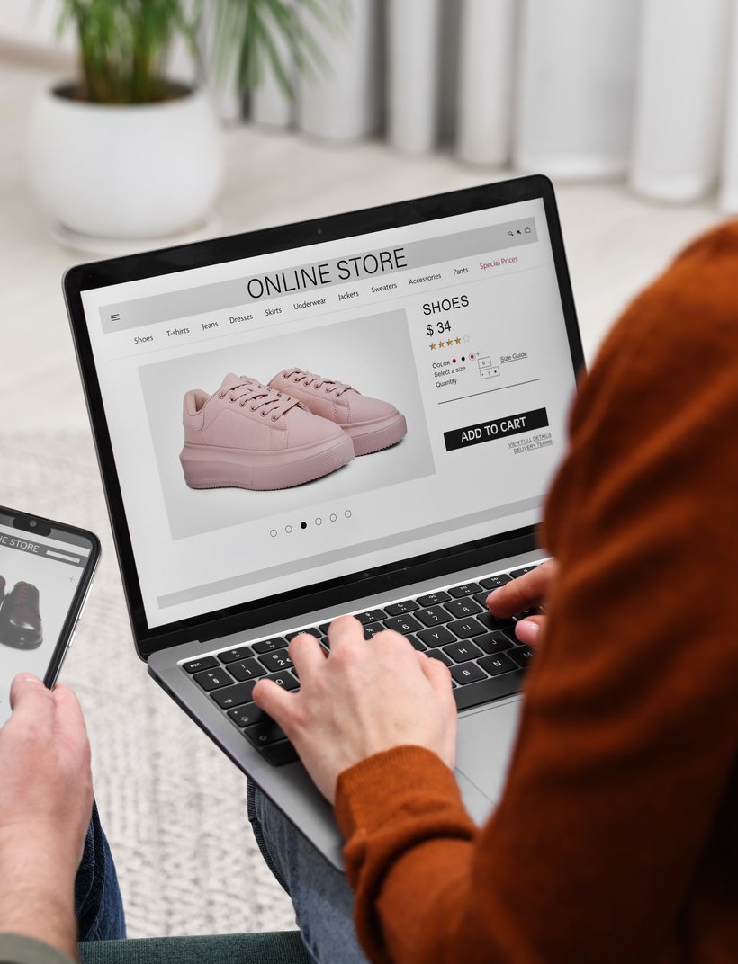 Two people shopping online for shoes, using a laptop and a smartphone. Pink sneakers displayed on the laptop screen.