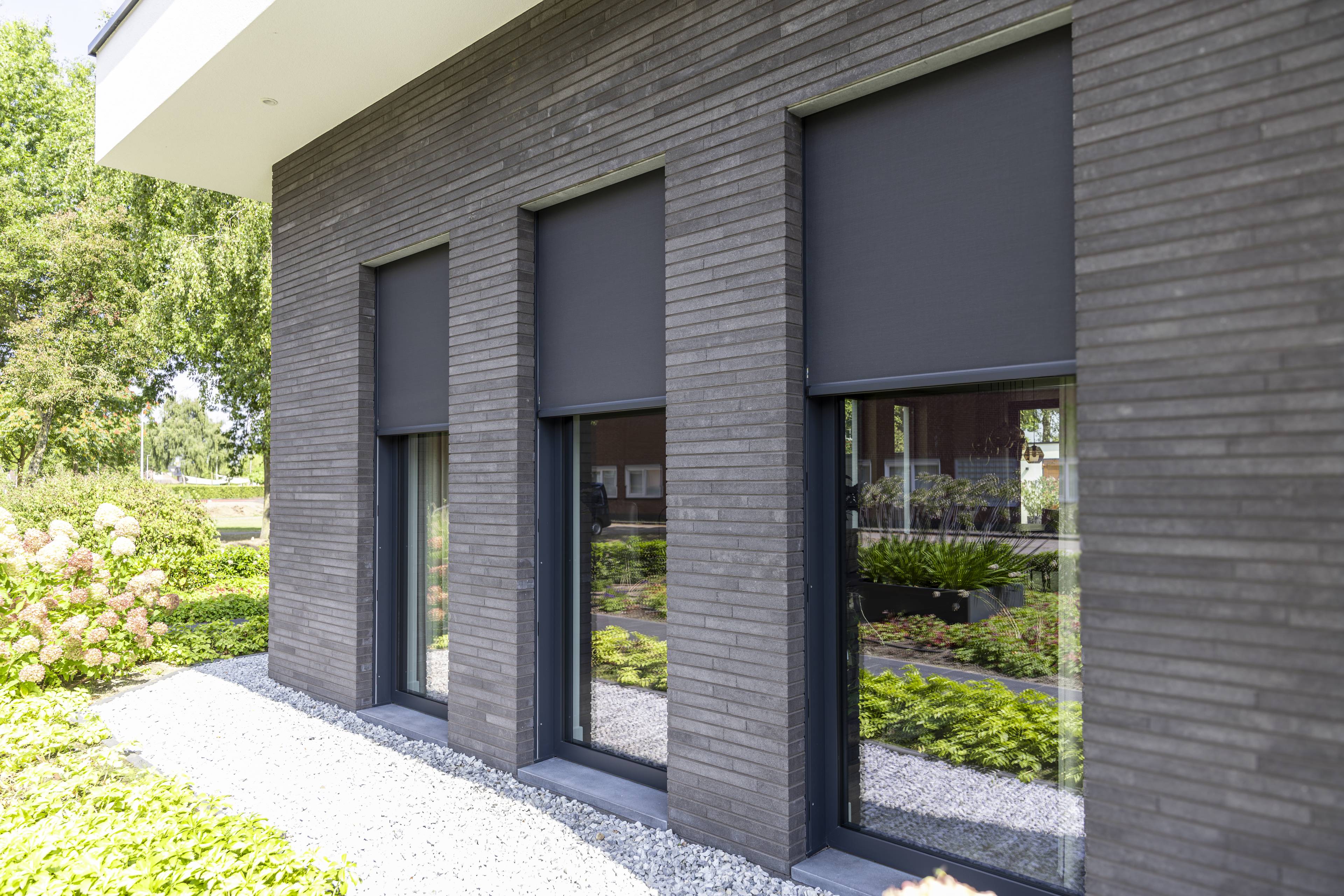 Maison moderne avec des fenêtres en aluminium noir et des stores screen foncés.