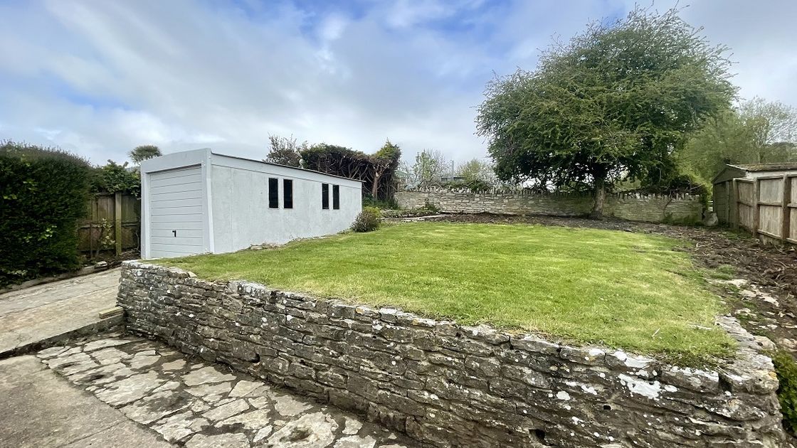 Garden with a wall up to grass area, small patio area and a garage on the left