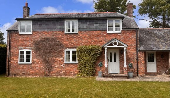 A red brick house with white-framed windows, ivy on the wall, and a grassy lawn under a partly cloudy sky.