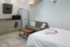 Cozy studio with a bed, small kitchen, sofa, and coffee table. Towels are neatly placed on the bed. Soft lighting creates a warm ambiance.