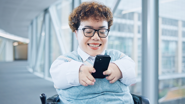 Smiling person in a wheelchair using a smartphone in a modern building