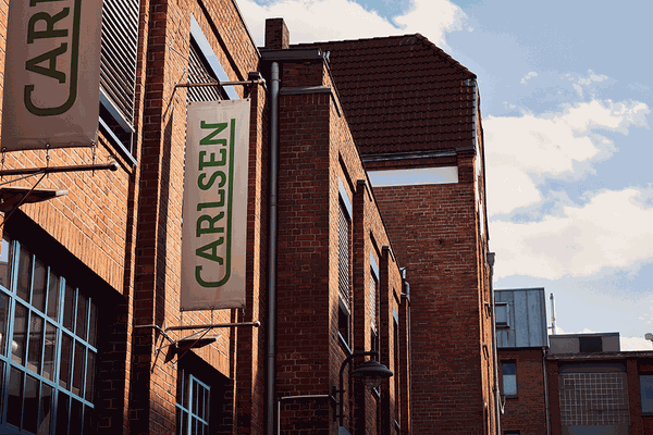 Brick building with "CARLSEN" banners, featuring large windows and a sloped roof, set against a partly cloudy sky.