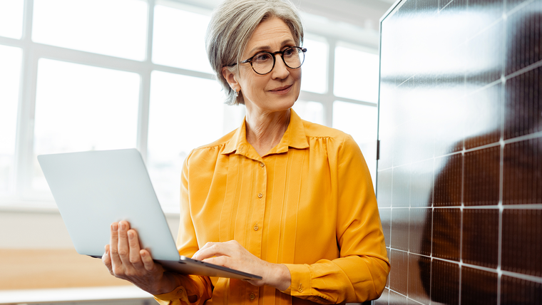 Woman with a laptop standing beside solar panels, analyzing data
