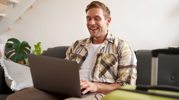 Man sitting on a sofa, smiling while working on a laptop