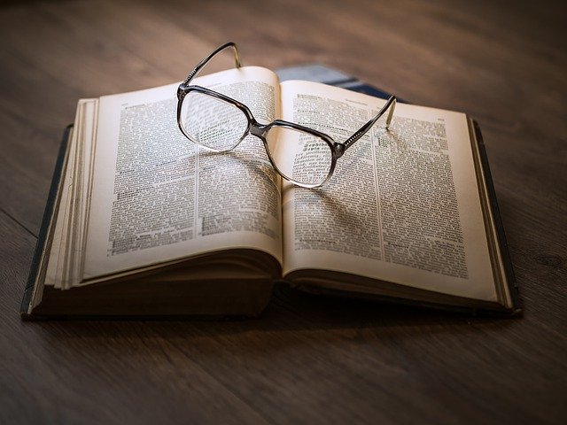 A pair of glasses lie on an open book.