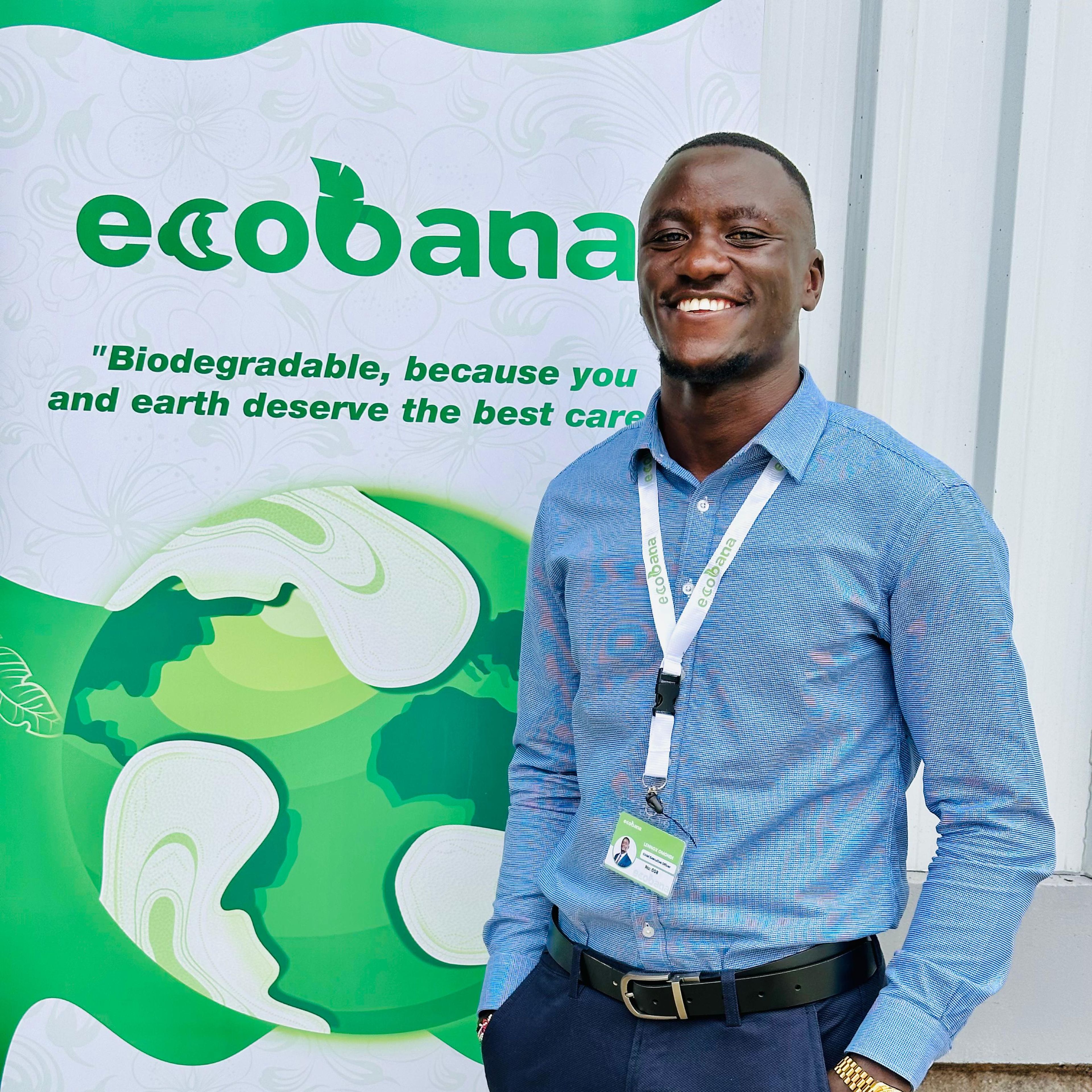 Smiling man in a blue shirt stands in front of an Ecobana banner promoting biodegradable products.