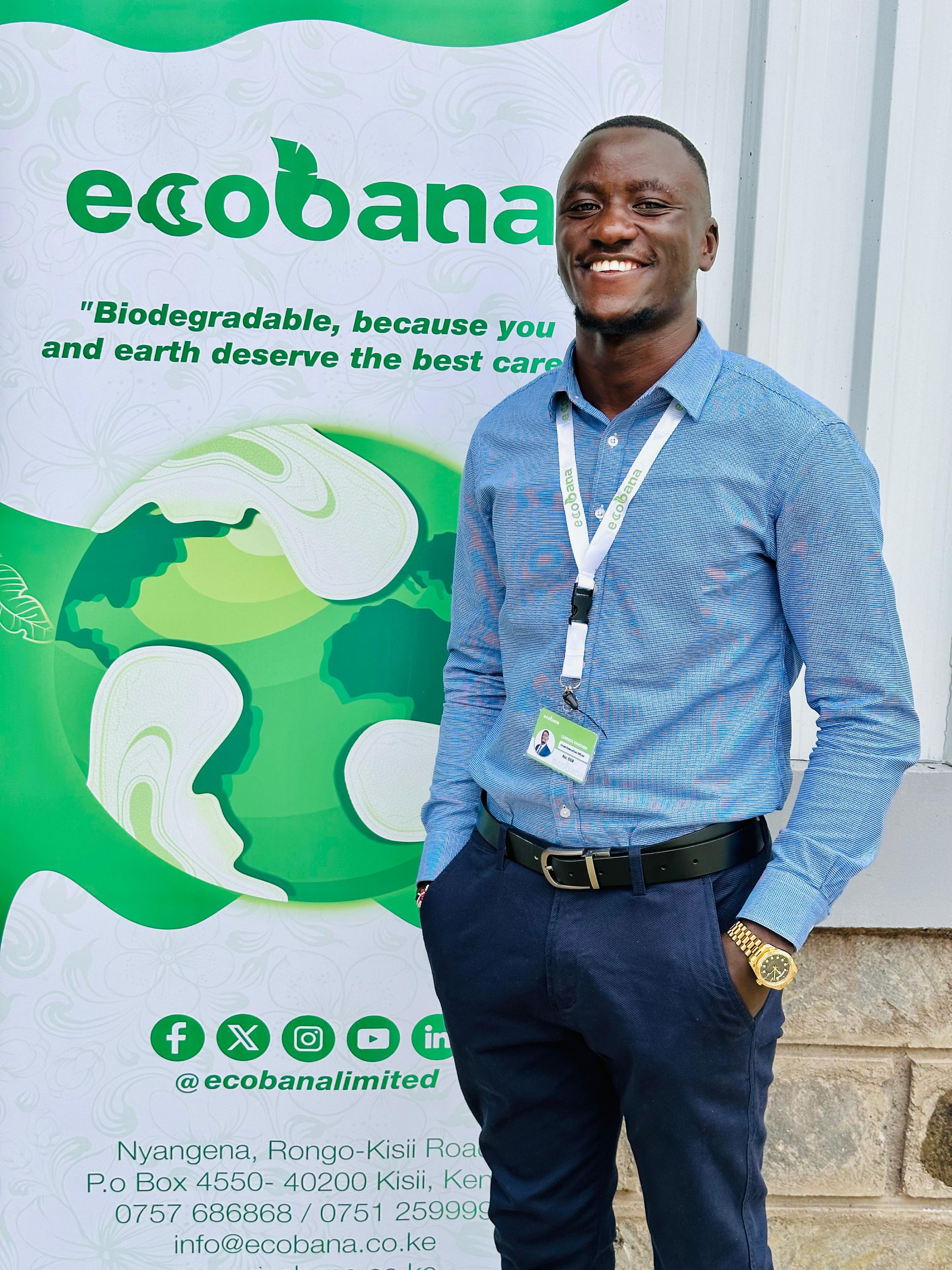 Smiling man in a blue shirt stands in front of an Ecobana banner promoting biodegradable products.
