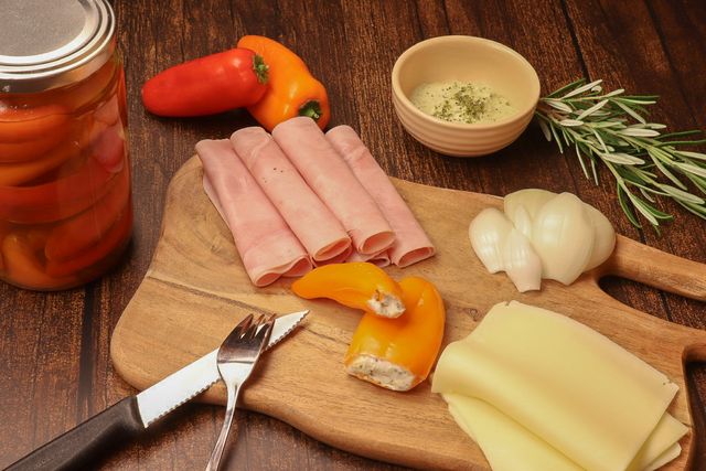 Eingelegte Minipaprika auf einem Holzbrett mit Wurst und Käse