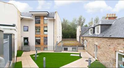 Modern building complex with a mix of stone and wood facade, surrounded by a courtyard with green artificial grass and paved walkways.