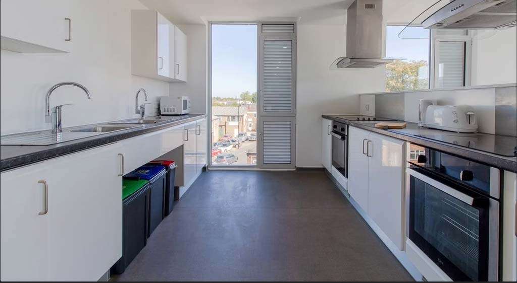 Modern kitchen with white cabinets, stainless steel appliances, and a large window. Two sinks, an oven, and a toaster are visible.