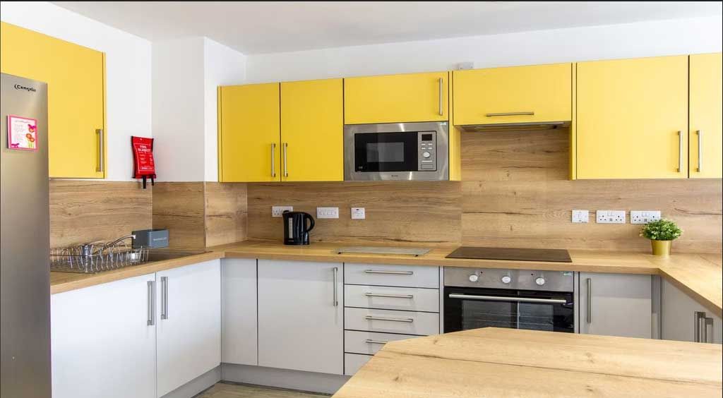 Modern kitchen with yellow and white cabinets, wood countertops, a stainless steel oven, microwave, and a small potted plant on the counter.