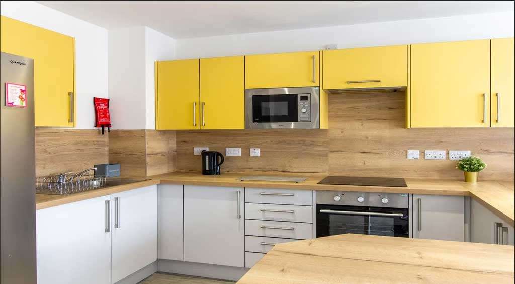 Modern kitchen with yellow and white cabinets, wood countertops, a stainless steel oven, microwave, and a small potted plant on the counter.