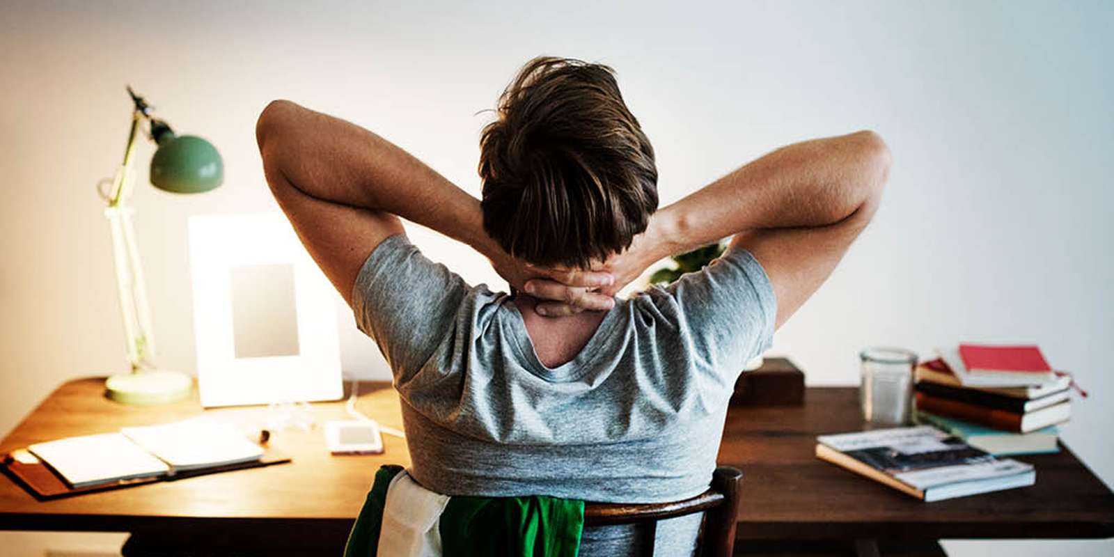 View of man from behind on his own at a desk stretching