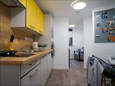 Modern kitchen with yellow cabinets, wooden countertop, and wall-mounted photos. A cozy living area is visible in the background.