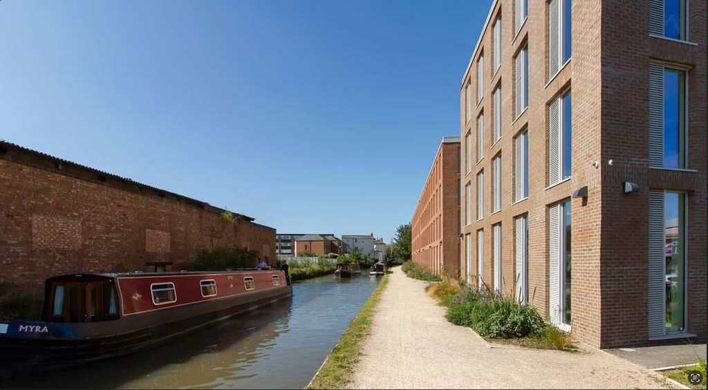 Narrowboat on a canal beside modern brick buildings under a clear blue sky.