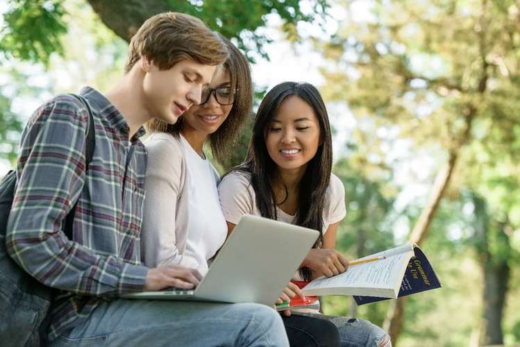 Group of students all looking at a laptop whilst taking notes