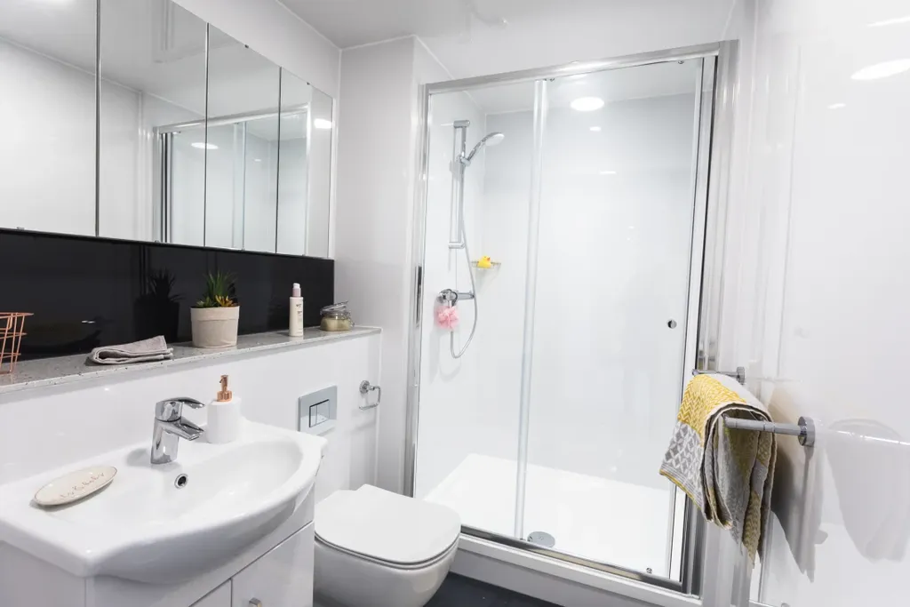 Modern bathroom with a white sink, toilet, glass-enclosed shower, mirrored cabinets, and towels on a rail. Minimalist decor with a plant.