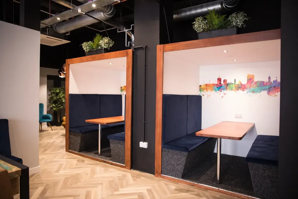 Modern café with two wooden booths, blue seating, and colorful wall art. Potted plants on top add greenery. Herringbone floor pattern.