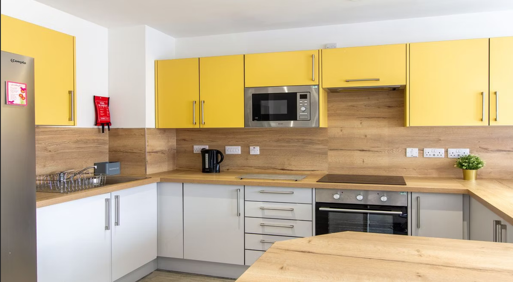 Modern kitchen with yellow and white cabinets, stainless steel appliances, wooden countertops, and a small potted plant on the counter.