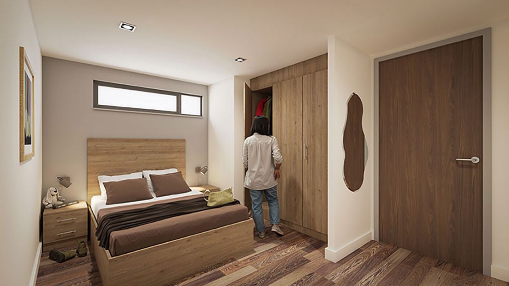Modern small bedroom with wooden bed and nightstand; a person seen from behind opening a built-in wardrobe.