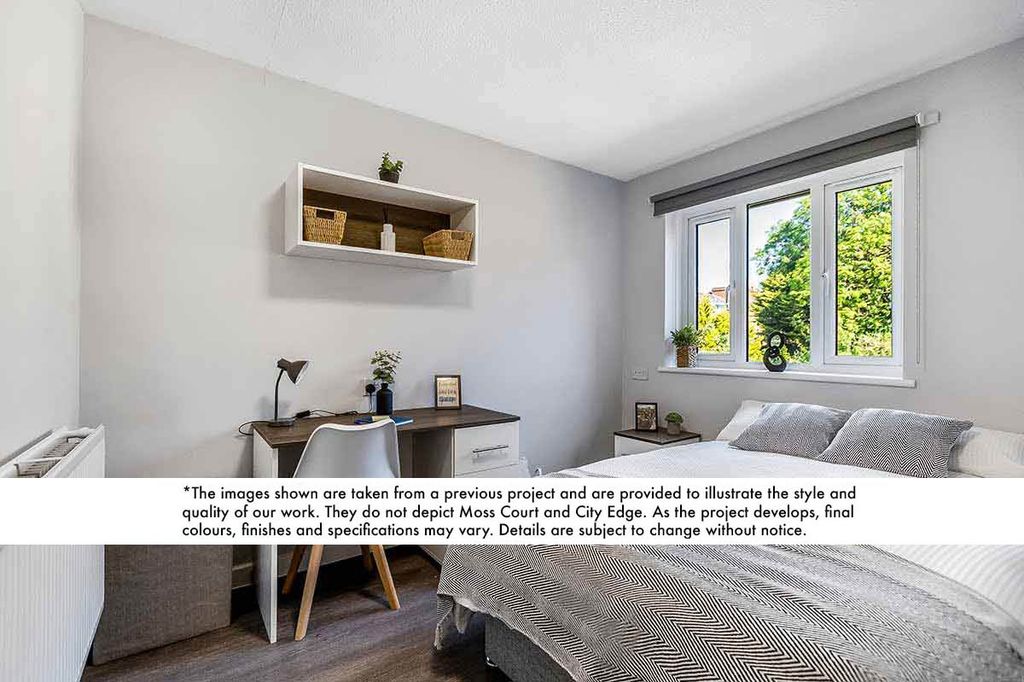 Minimalist bedroom with a desk, chair, and shelving. Bed with gray bedding beside a window showing greenery. Light walls and wooden flooring.