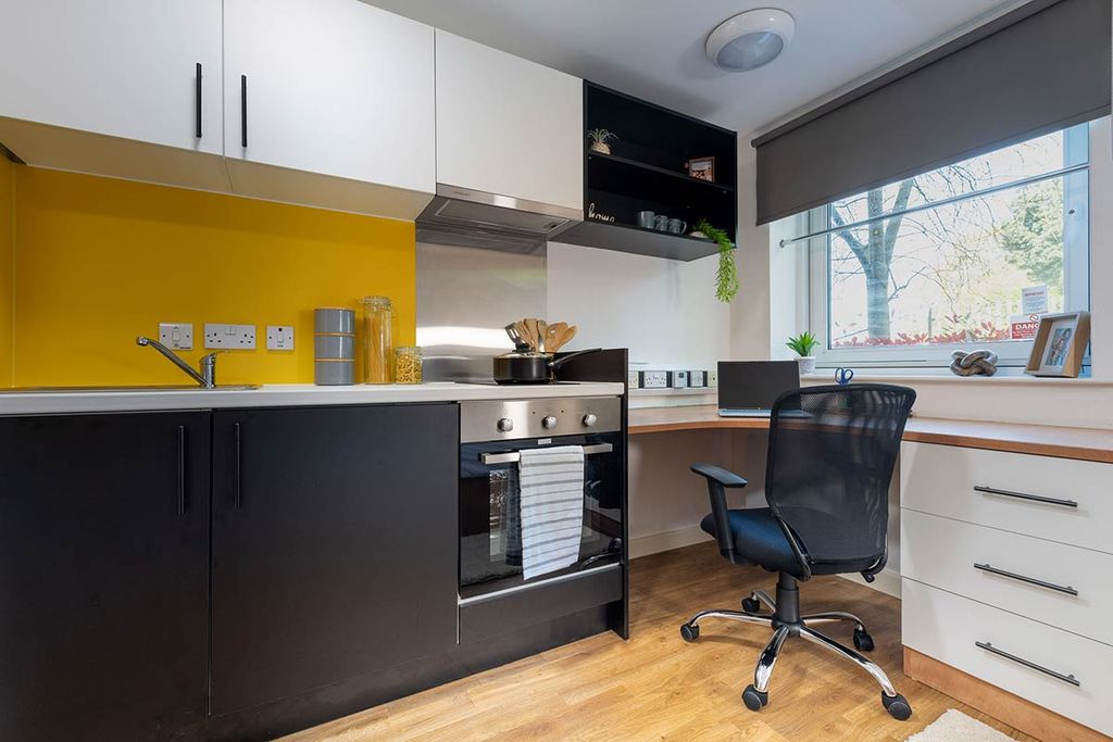 Modern kitchen with yellow backsplash, black and white cabinets, oven, and a workspace with laptop, chair, and window view.
