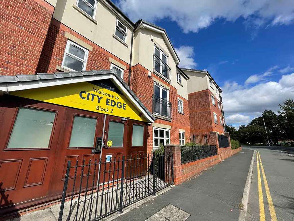 Apartment building with a red brick facade and a "Welcome to City Edge Block 2" sign. Clear blue sky and a road with yellow lines.