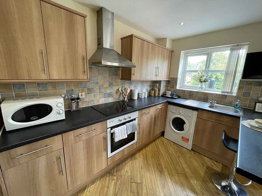 Modern kitchen with wooden cabinets, black countertops, stainless steel appliances, a washing machine, and a small dining area by the window.